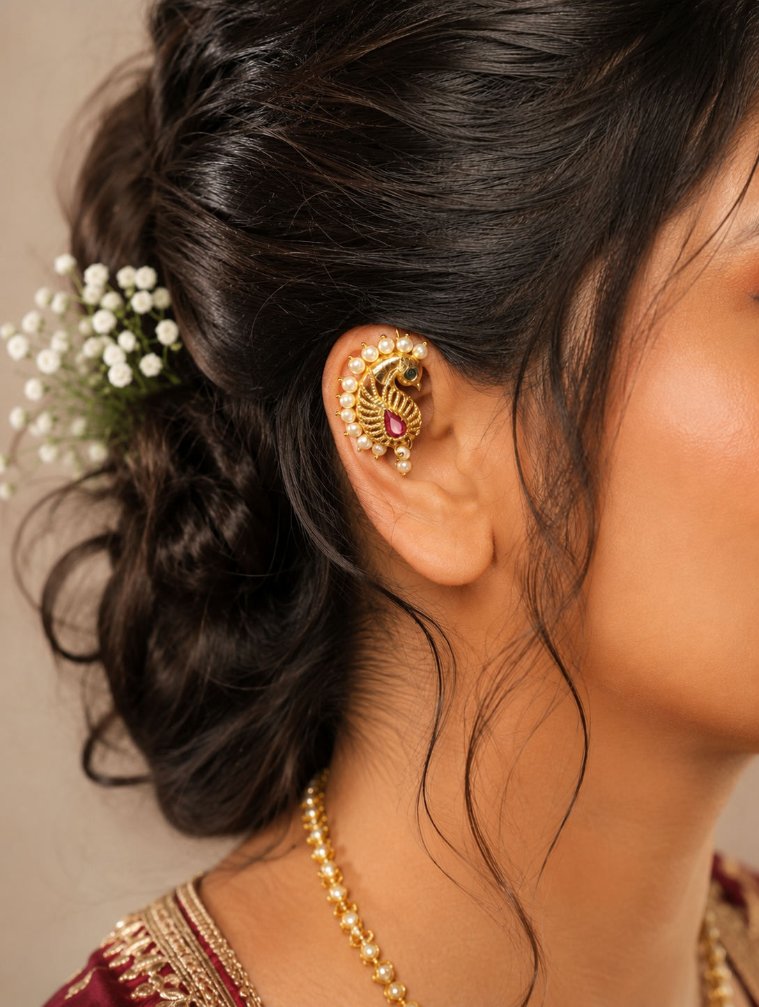 Side profile view of a model wearing a traditional gold-plated peacock ear cuff, beautifully curved along the outer cartilage edge of the ear, adorned with a red teardrop stone and pearl border accents, styled with a formal updo.