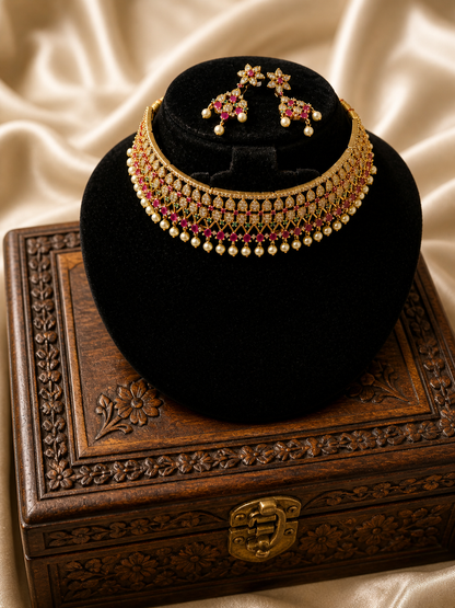 A beautiful antique gold-plated kemp choker necklace and matching floral drop earrings displayed on a black velvet stand. The necklace features an openwork lattice pattern set with white CZ and ruby red stones, finished with small dangling pearls.