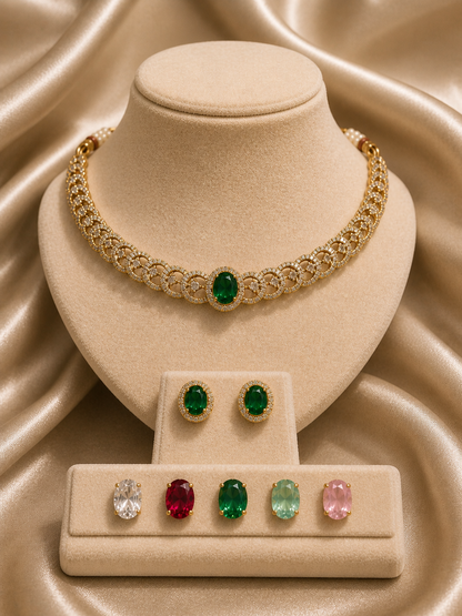 A gold-plated choker necklace and matching stud earrings set displayed on a beige stand, featuring a lattice pattern lined with white CZ stones and an interchangeable oval emerald green center stone, shown alongside five alternative replacement stones in clear, ruby red, dark green, mint green, and light pink.