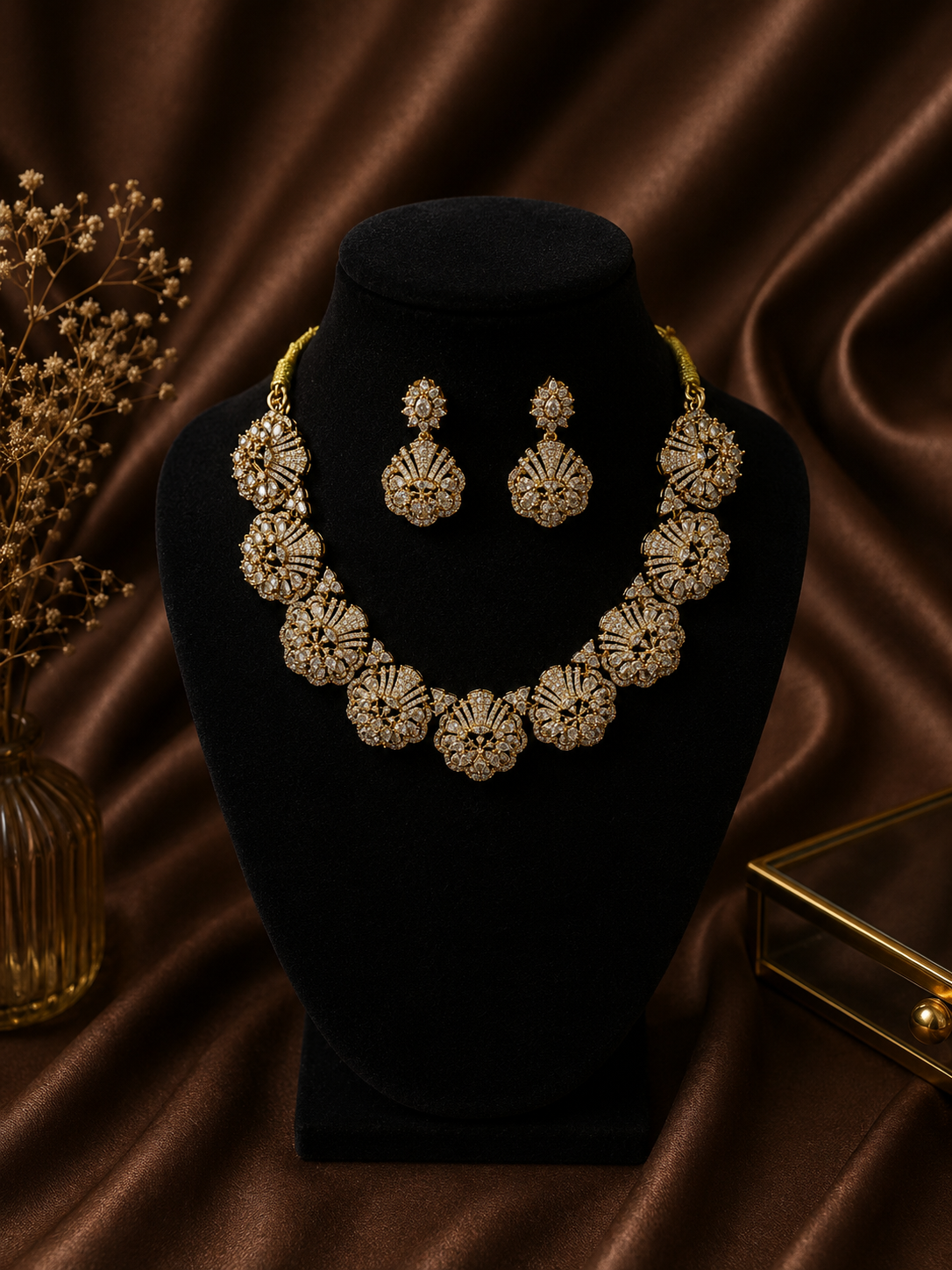 A premium gold-plated bridal jewelry set displayed on a rich brown satin fabric, featuring a thick choker necklace made of large, interconnected circular floral motifs densely packed with uncut white AD stones, paired with matching statement drop earrings.