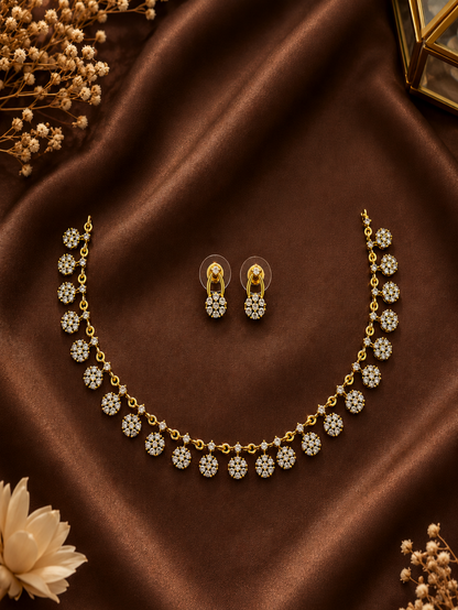 Dainty gold-plated necklace featuring a continuous row of small, dangling floral cluster charms set with clear cubic zirconia crystals, displayed on a black matte bust stand.