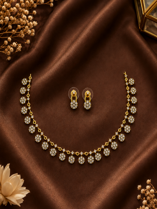 Dainty gold-plated necklace featuring a continuous row of small, dangling floral cluster charms set with clear cubic zirconia crystals, displayed on a black matte bust stand.