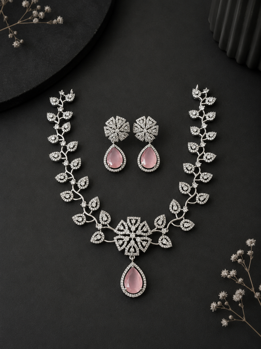 A silver-toned floral necklace and matching earrings set featuring crystal-studded leaves and prominent pink teardrop gemstones, displayed on a sleek black background.