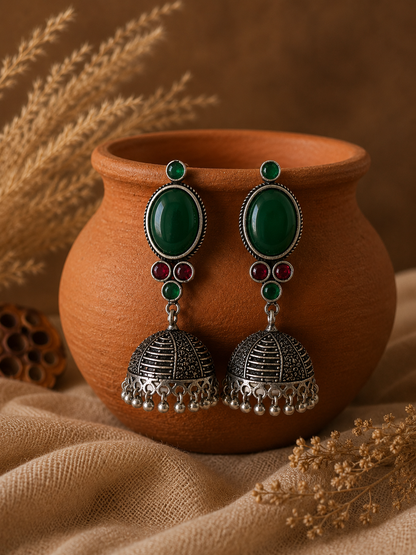 Ornate earrings with green and red stones on a terracotta pot with dried plants.