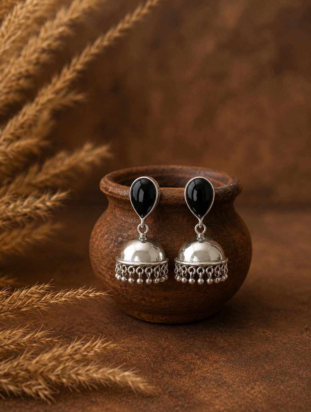 Silver earrings with black stones on a brown ceramic pot against a brown background