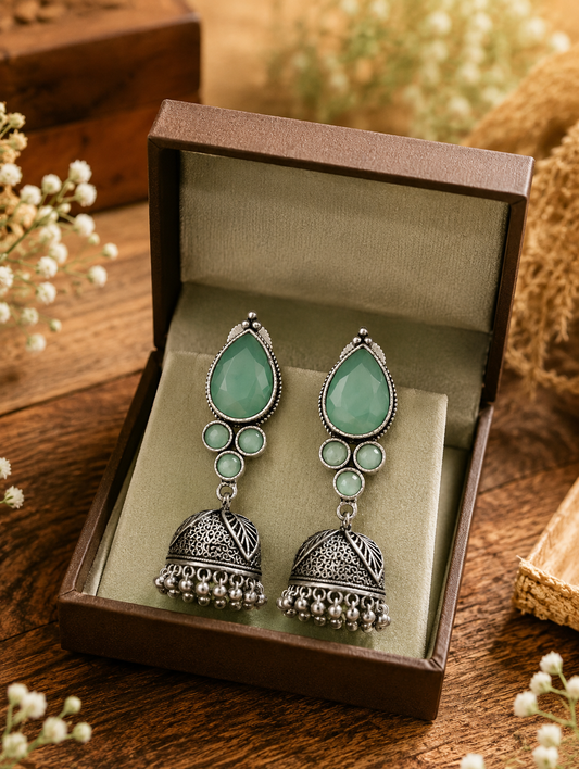 A pair of oxidized silver Jhumka earrings set with mint green teardrop and round stones, presented inside an open brown jewelry gift box as shown 