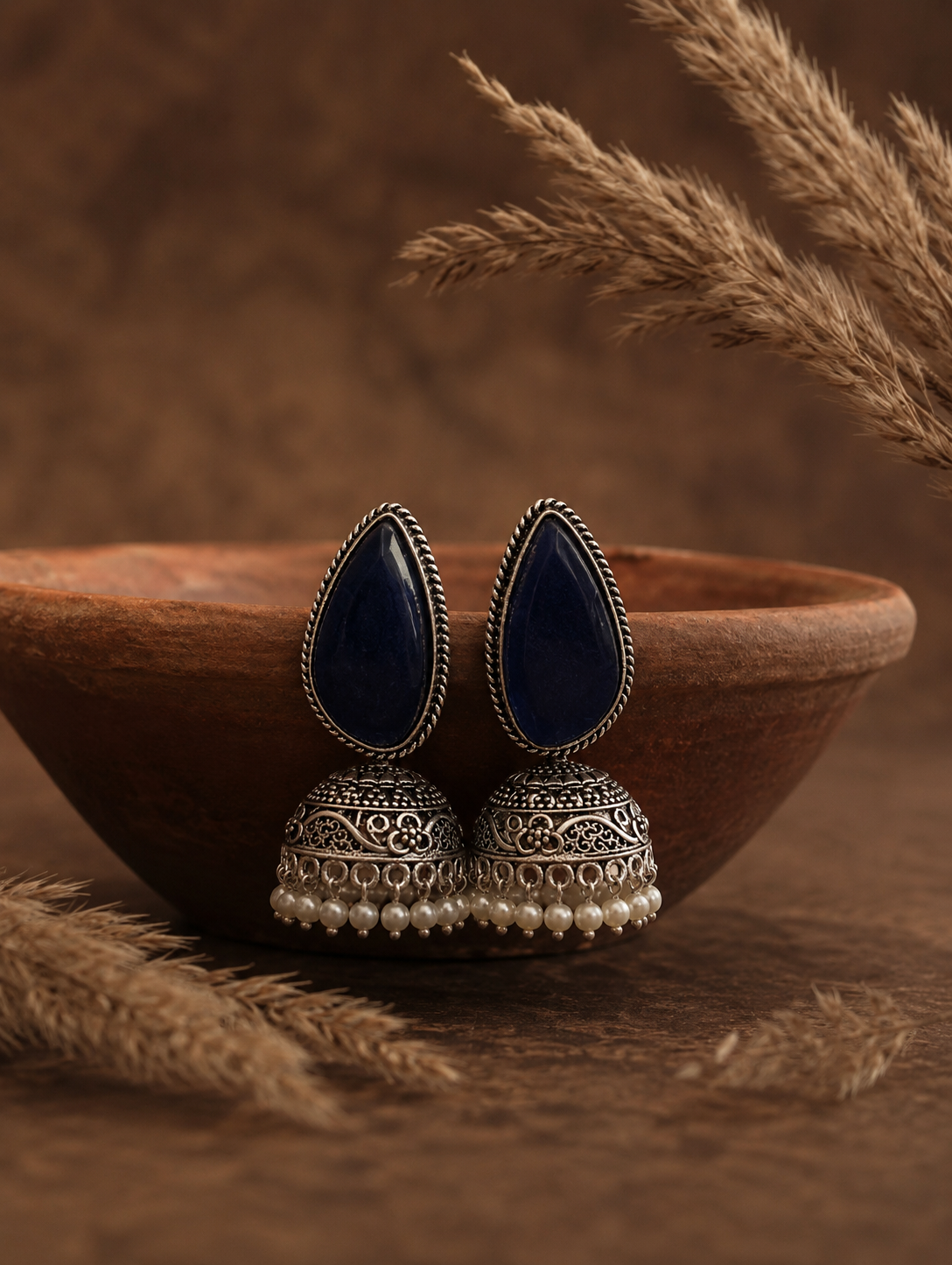 Pair of blue teardrop earrings with silver and pearl detailing in a wooden bowl on a brown background.