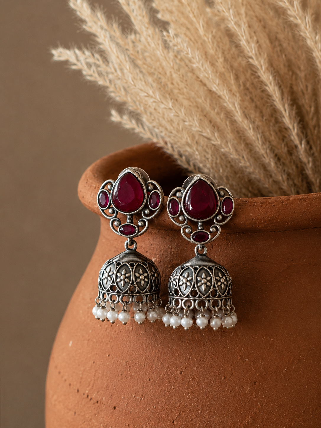 Silver earrings with red gemstones and pearl-like beads on a terracotta surface.