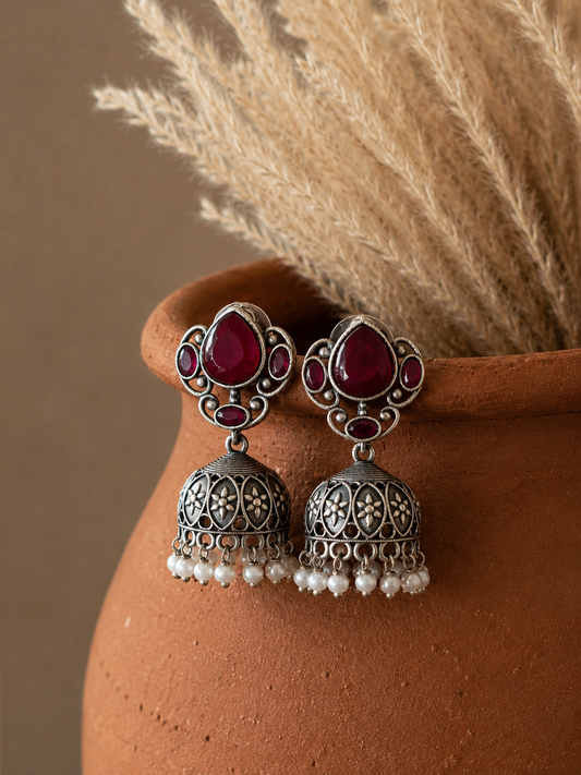 Silver earrings with red gemstones and pearl-like beads on a terracotta surface.