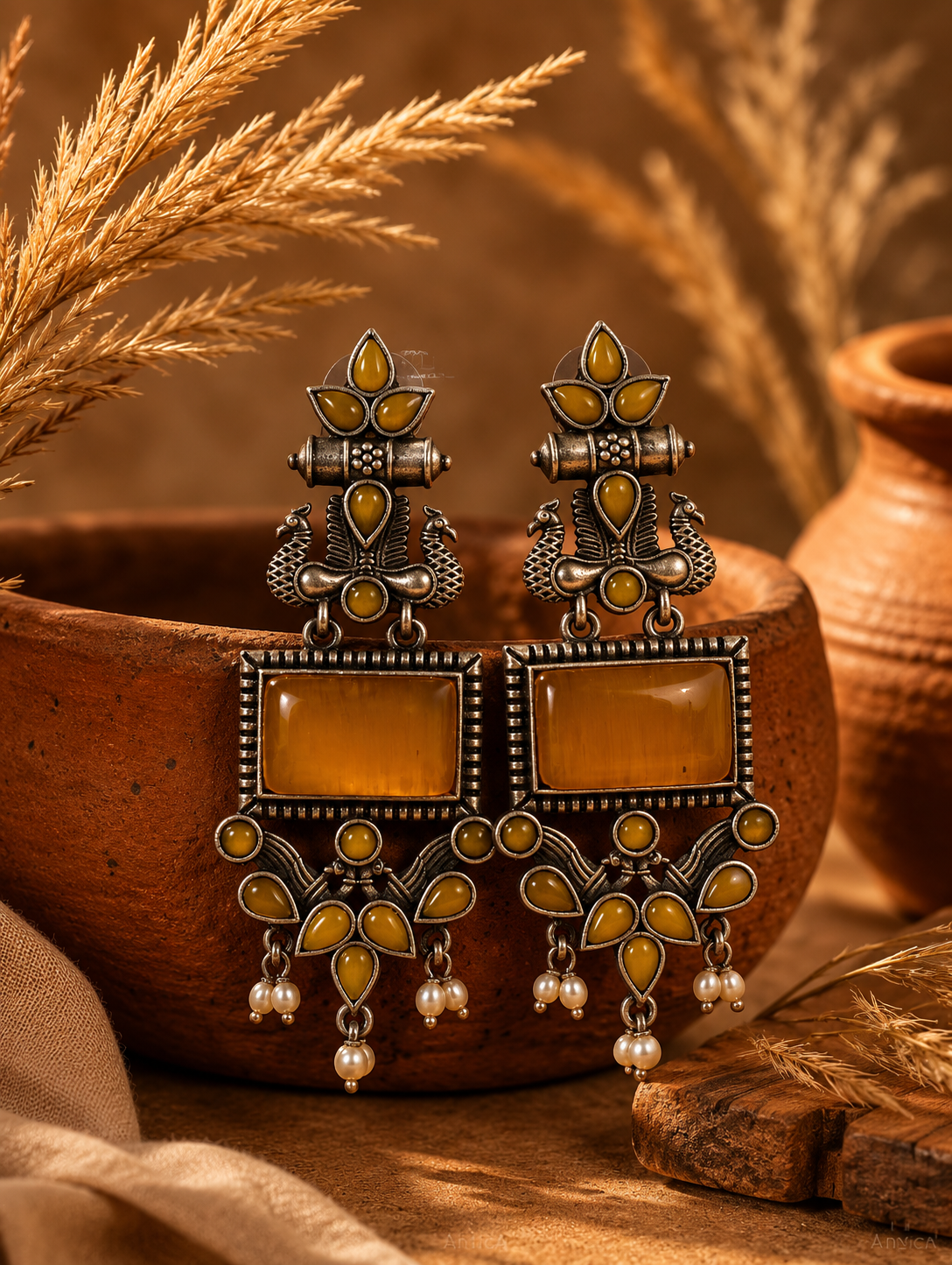 A pair of Mayurika oxidized silver statement earrings decorated with detailed twin peacock motifs, large rectangular mustard yellow stones, and hanging pearl clusters.