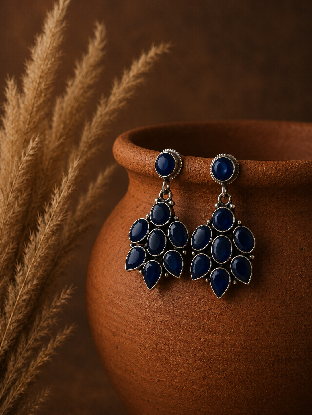 Blue earrings with gold accents on a brown vase against a brown background