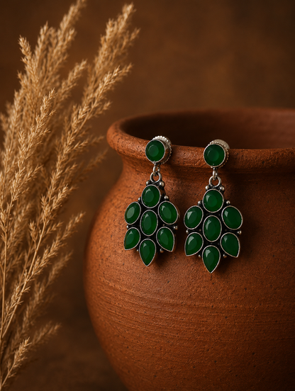 A pair of Lancy oxidized silver drop earrings featuring a round green gemstone stud and a tiered chandelier cluster of teardrop-shaped green stones, hanging from a clay pot.