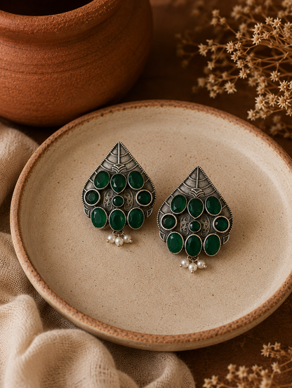 Pair of green and silver earrings on a beige plate with a brown background