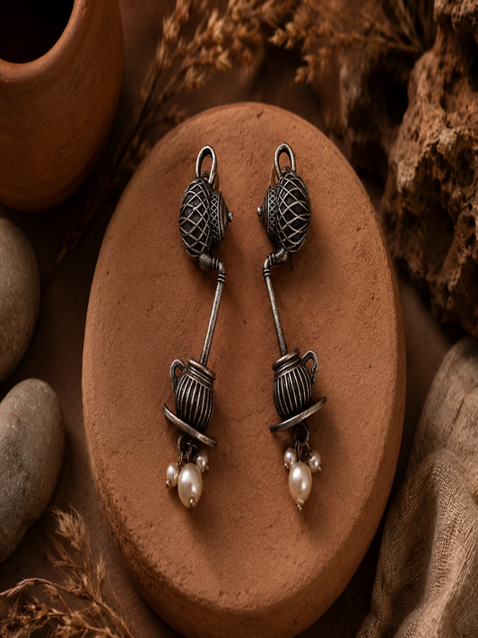 A pair of Smitha oxidized silver novelty dangle earrings featuring a patterned teapot pouring down into a ribbed teacup on a saucer, accented with hanging pearls.