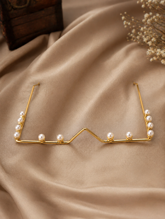 Minimalist gold wire facial frame accessory shaped like glasses, studded with luminous pearls along the lower rim and temples, displayed on a soft beige fabric background and worn by a smiling model in traditional attire.