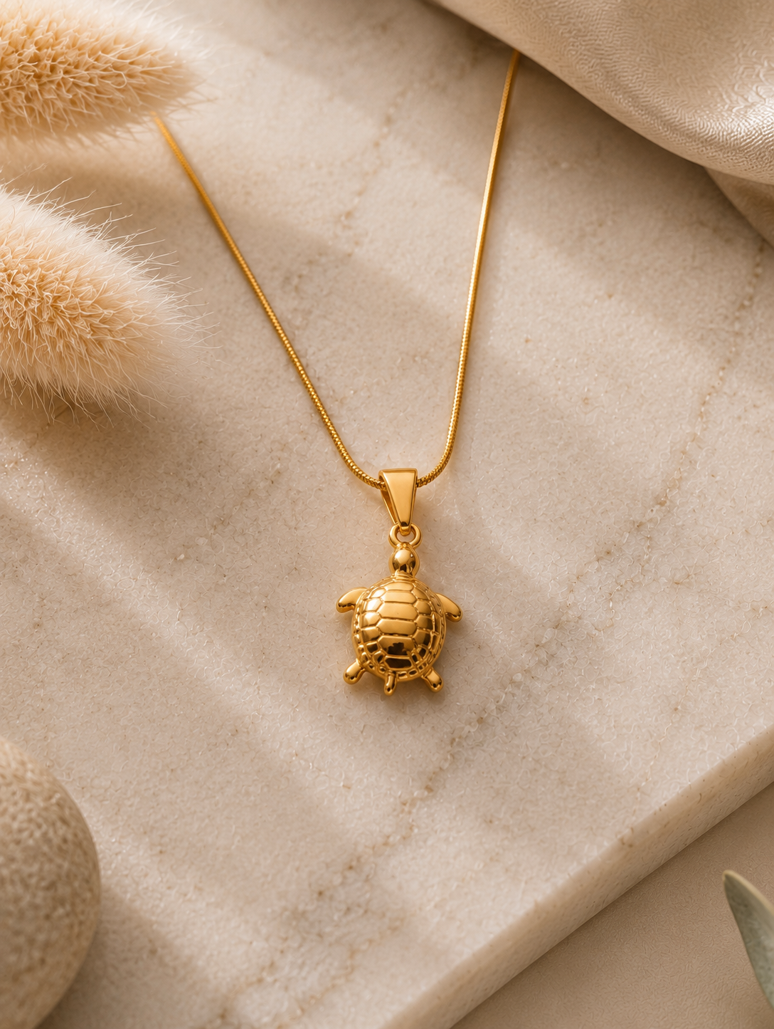 A close-up of a woman wearing a delicate gold necklace featuring a detailed turtle pendant with an engraved shell, draped elegantly against her collarbone while wearing a ribbed, off-the-shoulder brown top. Stainless Steel.