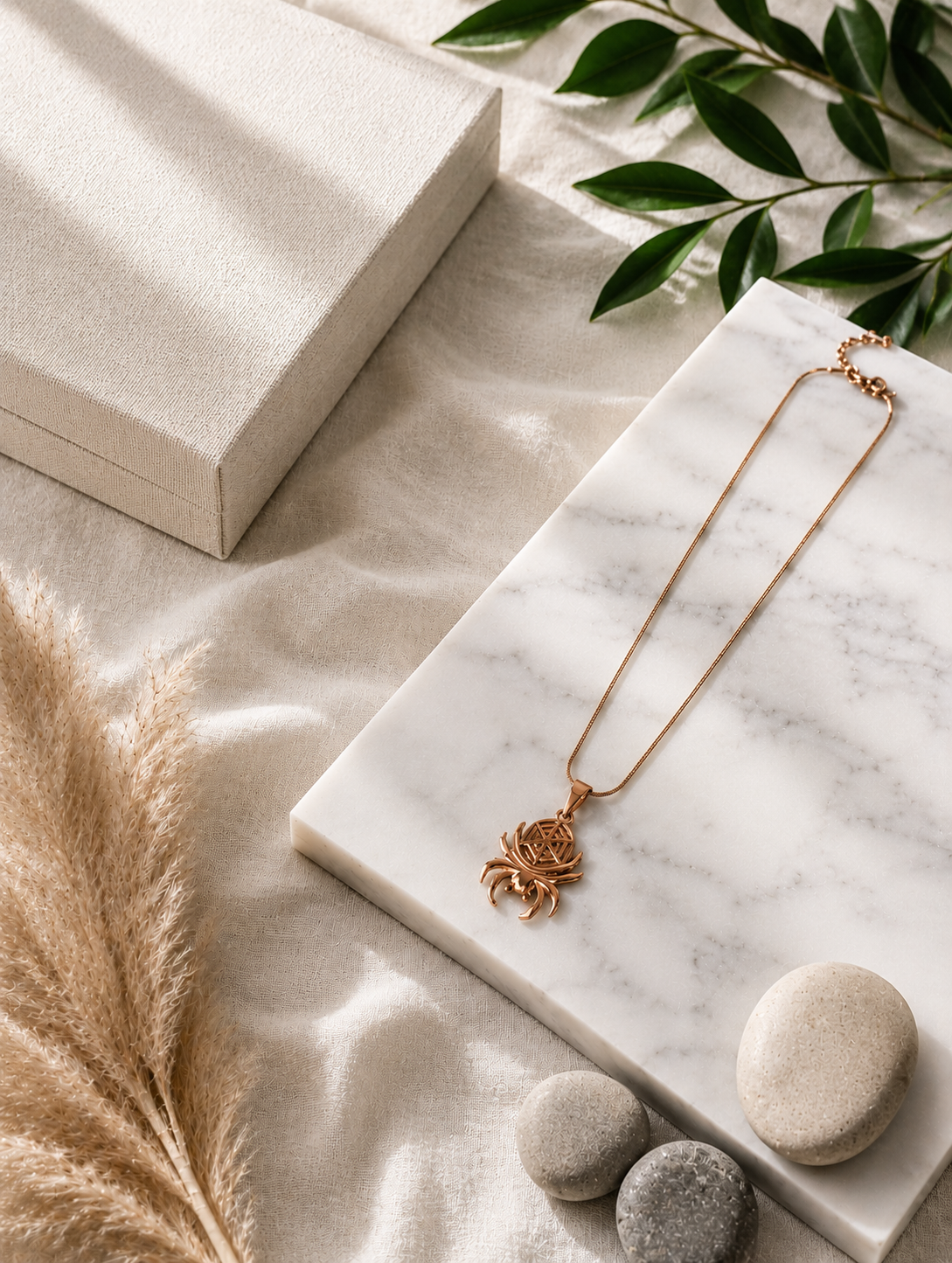A polished rose gold-toned pendant necklace shaped like a spider, featuring curved legs and an intricate geometric web design cutout on the body. The pendant hangs from a thin, smooth snake chain and is displayed both as an aesthetic flat-lay on a white marble surface and draped over a neutral jewelry mannequin bust.