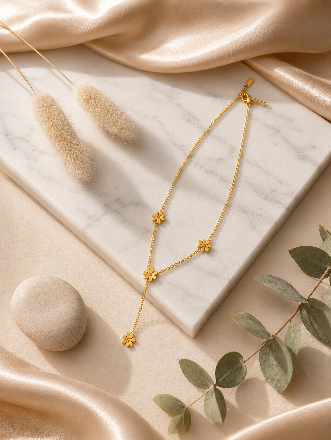 A gold-toned Y-necklace featuring spaced daisy flower stations, each accented with a central crystal. The necklace is showcased through a mix of lifestyle and product photography, including a marble flat lay and a model shot.