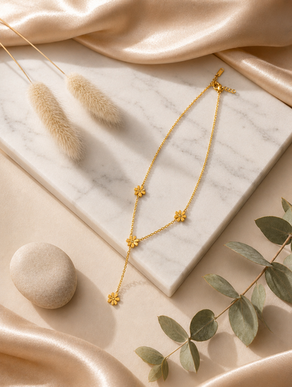 A gold-toned Y-necklace featuring spaced daisy flower stations, each accented with a central crystal. The necklace is showcased through a mix of lifestyle and product photography, including a marble flat lay and a model shot.