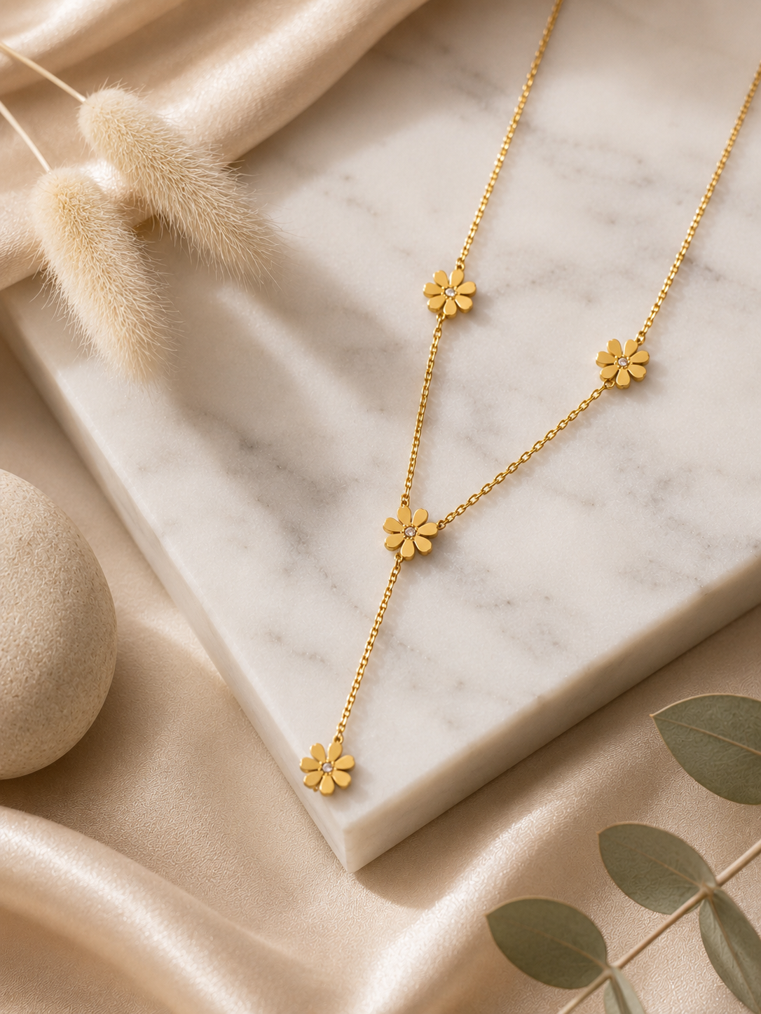 A gold-toned Y-necklace featuring spaced daisy flower stations, each accented with a central crystal. The necklace is showcased through a mix of lifestyle and product photography, including a marble flat lay and a model shot.
