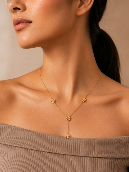 A gold-toned Y-necklace featuring spaced daisy flower stations, each accented with a central crystal. The necklace is showcased through a mix of lifestyle and product photography, including a marble flat lay and a model shot.