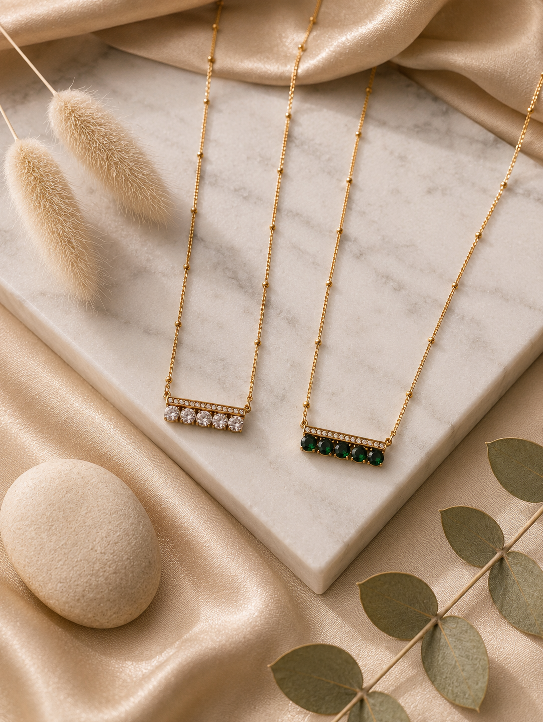A collection of lifestyle and product photos displaying two variants of a gold-toned horizontal bar pendant necklace. The pendant features a thin top bar lined with tiny sparkling crystals, with a row of five larger round stones set side-by-side underneath. One variant features clear, brilliant crystals, while the other features rich emerald-green stones. The necklaces are styled on a delicate station chain with small bead accents, shown both worn individually on a model's collarbone and laid out together o