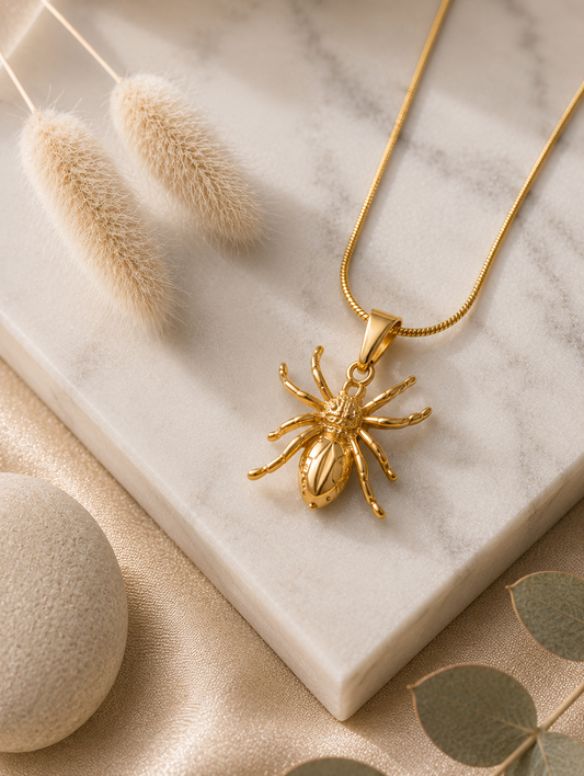 A collection of three product photographs showcasing a detailed gold-tone spider pendant necklace on a fine snake chain, styled in both a warm flat lay on a white marble slab and displayed on a beige velvet jewelry bust.