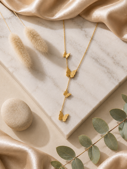 > A collection of three product photographs showcasing a delicate gold-tone Y-lariat chain necklace with four cascading, intricately textured butterfly charms, featured as a flat lay on marble (**GN027_butterfly chain.png**), on a velvet display bust (**GN027_butterfly chain_350.png**), and modeled on a woman's neckline (**GN027_butterfly chain_a.png**).