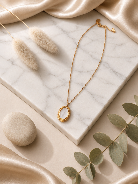 A close-up photograph from GN028_white milky pendent_399.png showing a woman wearing a delicate gold chain necklace with a vintage-inspired oval pendant, which features a smooth, milky-white stone framed by a textured, braided gold-tone border.