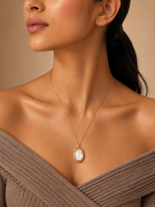 A close-up photograph from GN028_white milky pendent_399.png showing a woman wearing a delicate gold chain necklace with a vintage-inspired oval pendant, which features a smooth, milky-white stone framed by a textured, braided gold-tone border.