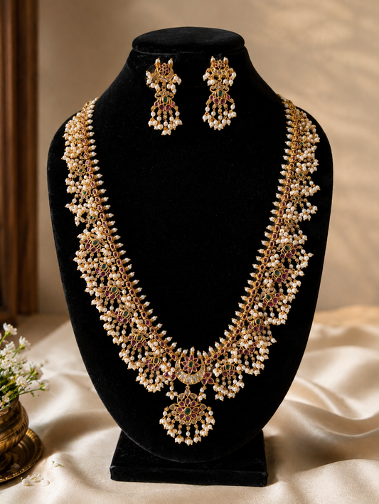 The Revathy Long Guttapusalu haram jewelry set displayed on a premium black velvet bust mannequin, featuring the long traditional necklace and a pair of matching floral drop earrings with cascading white pearls.