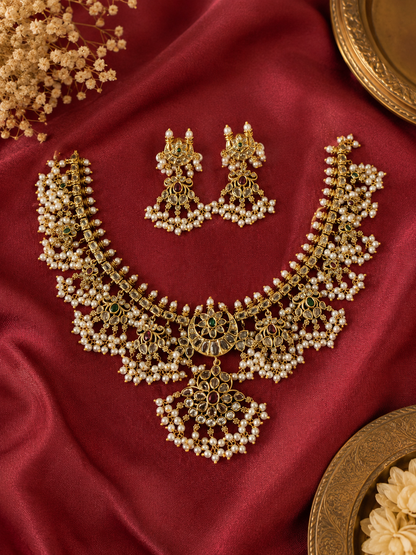 A flat lay view of the Bhavishya Guttapusalu jewelry set resting on a rich crimson silk fabric backdrop, detailed alongside decorative brass plates and delicate white floral accents.