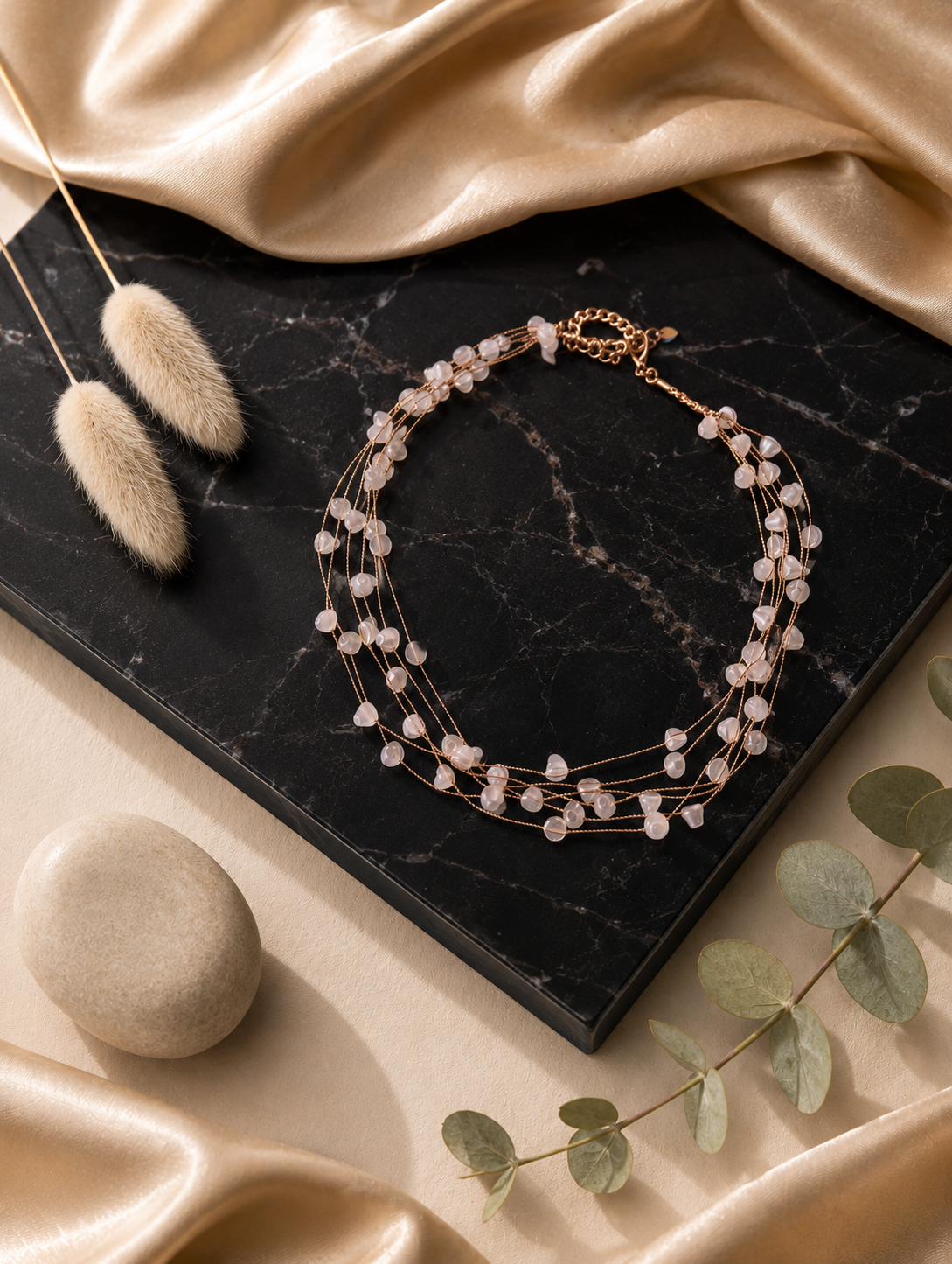 A close-up product photograph from GS003_pearl necklace_399.png showing a woman wearing a delicate, multi-strand gold necklace adorned with luminous, organically shaped white pearls, captured against a warm, sunlit beach backdrop.