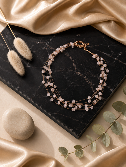 A close-up product photograph from GS003_pearl necklace_399.png showing a woman wearing a delicate, multi-strand gold necklace adorned with luminous, organically shaped white pearls, captured against a warm, sunlit beach backdrop.