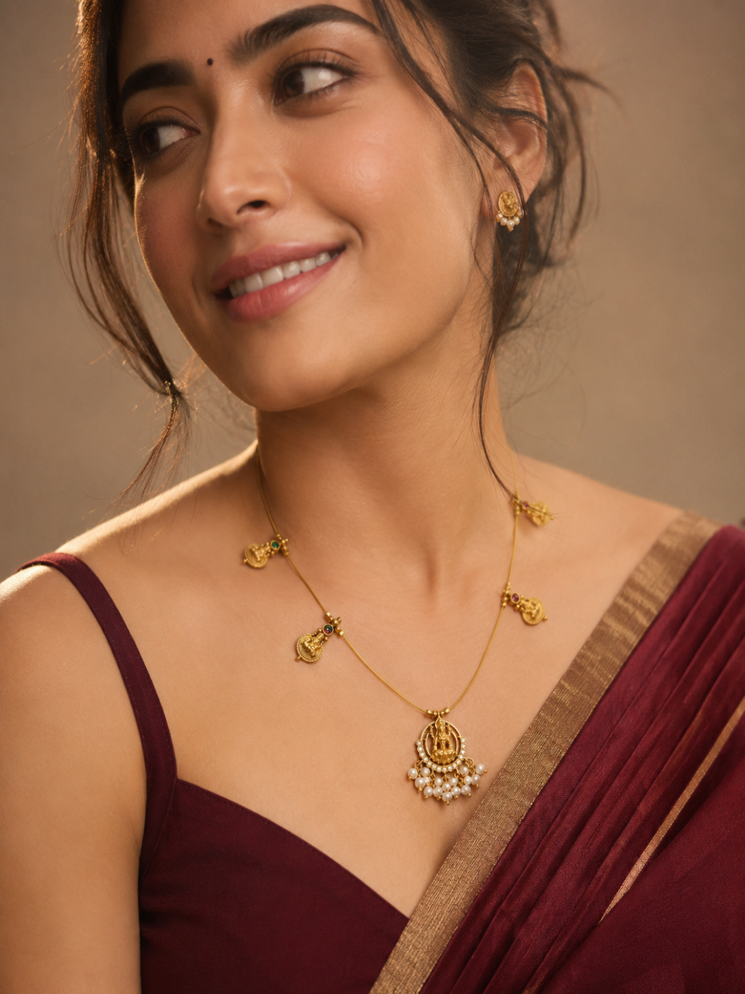 Woman wearing gold jewelry with a maroon saree against a neutral background