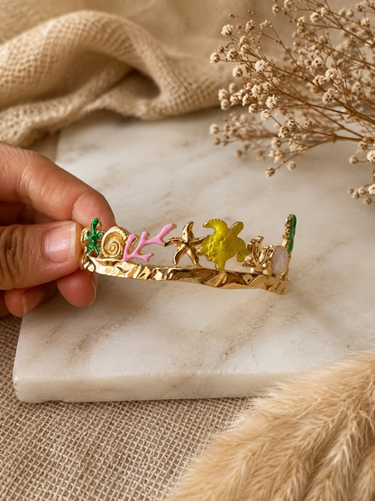 Gold tiara with colorful decorations held by a hand on a marble surface.