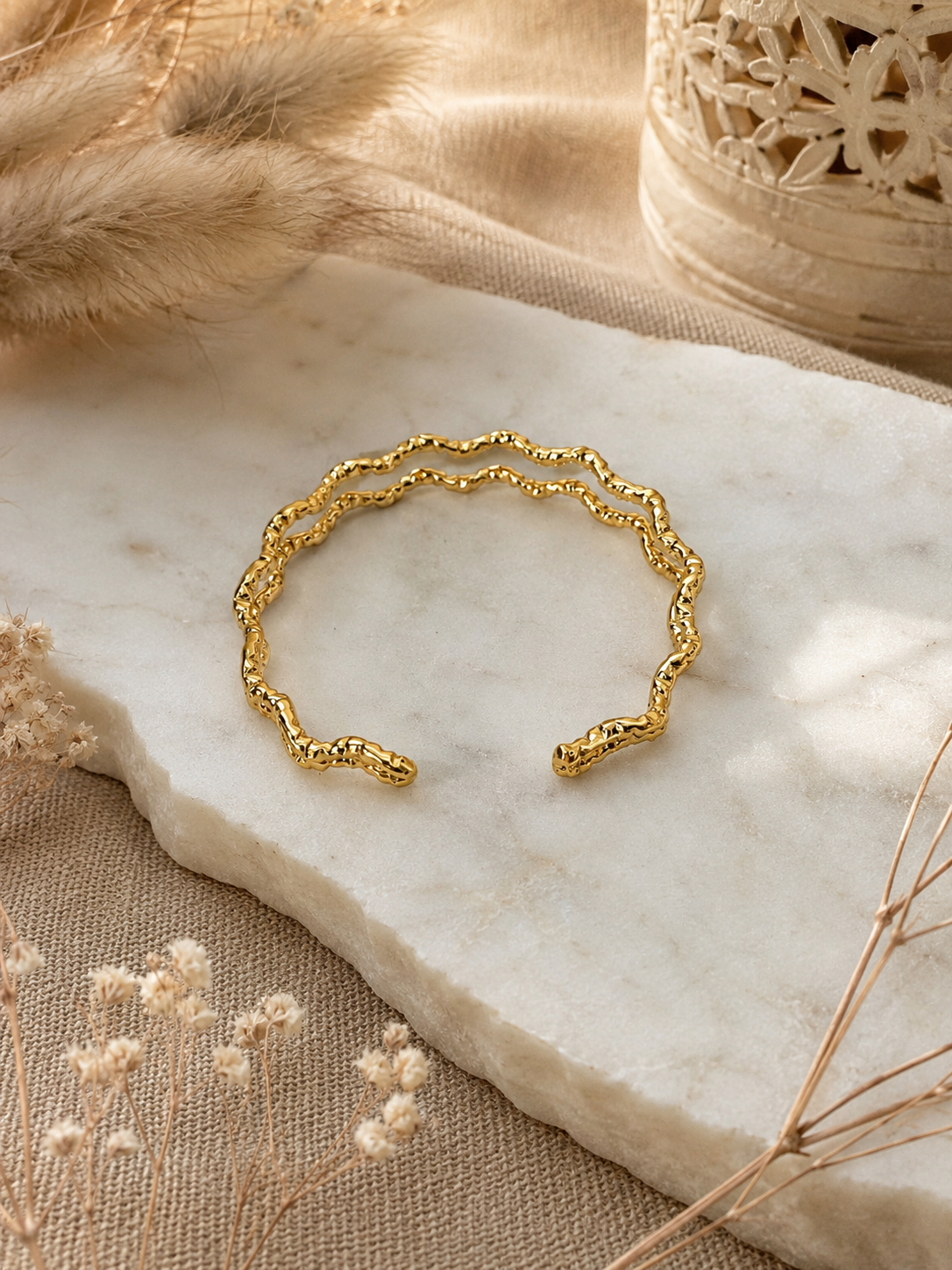 Gold bracelet on a marble surface with natural elements