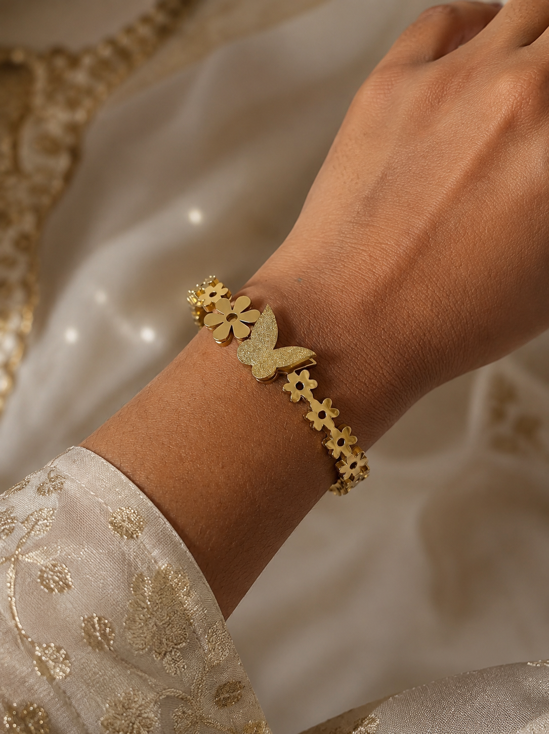 Gold bracelet with floral designs on a wrist against a soft, neutral background