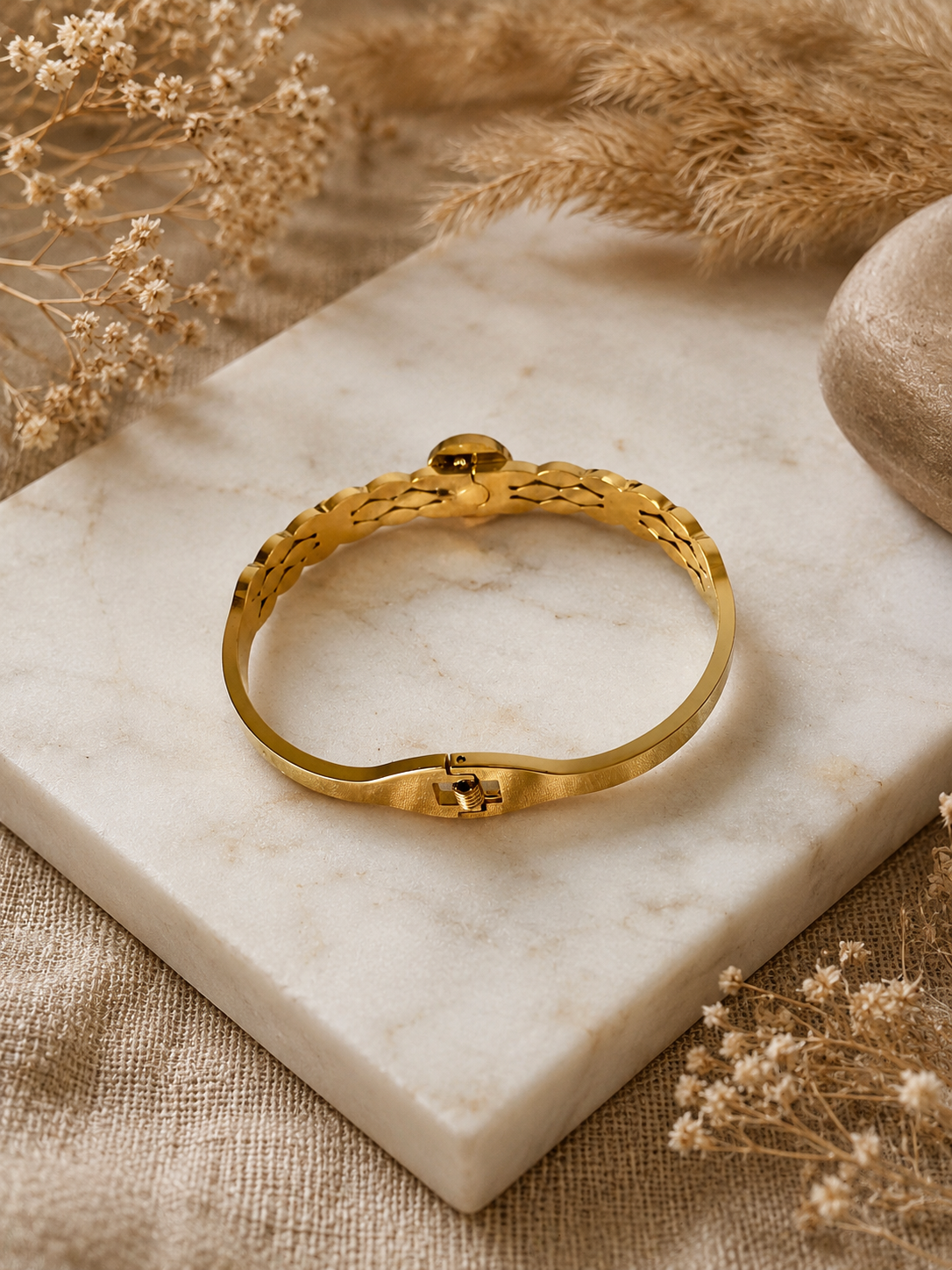 Gold bracelet on a marble surface with dried flowers and fabric