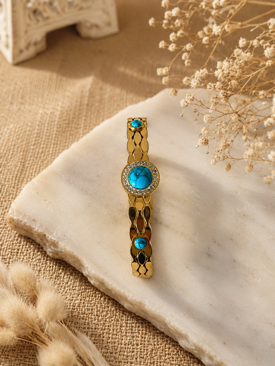Gold bracelet with turquoise stones on a stone surface with dried flowers