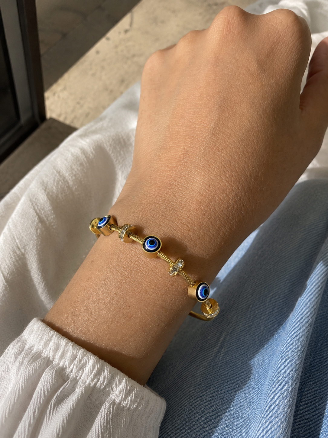 Bracelet with blue eye beads on a wrist, wearing a white shirt.