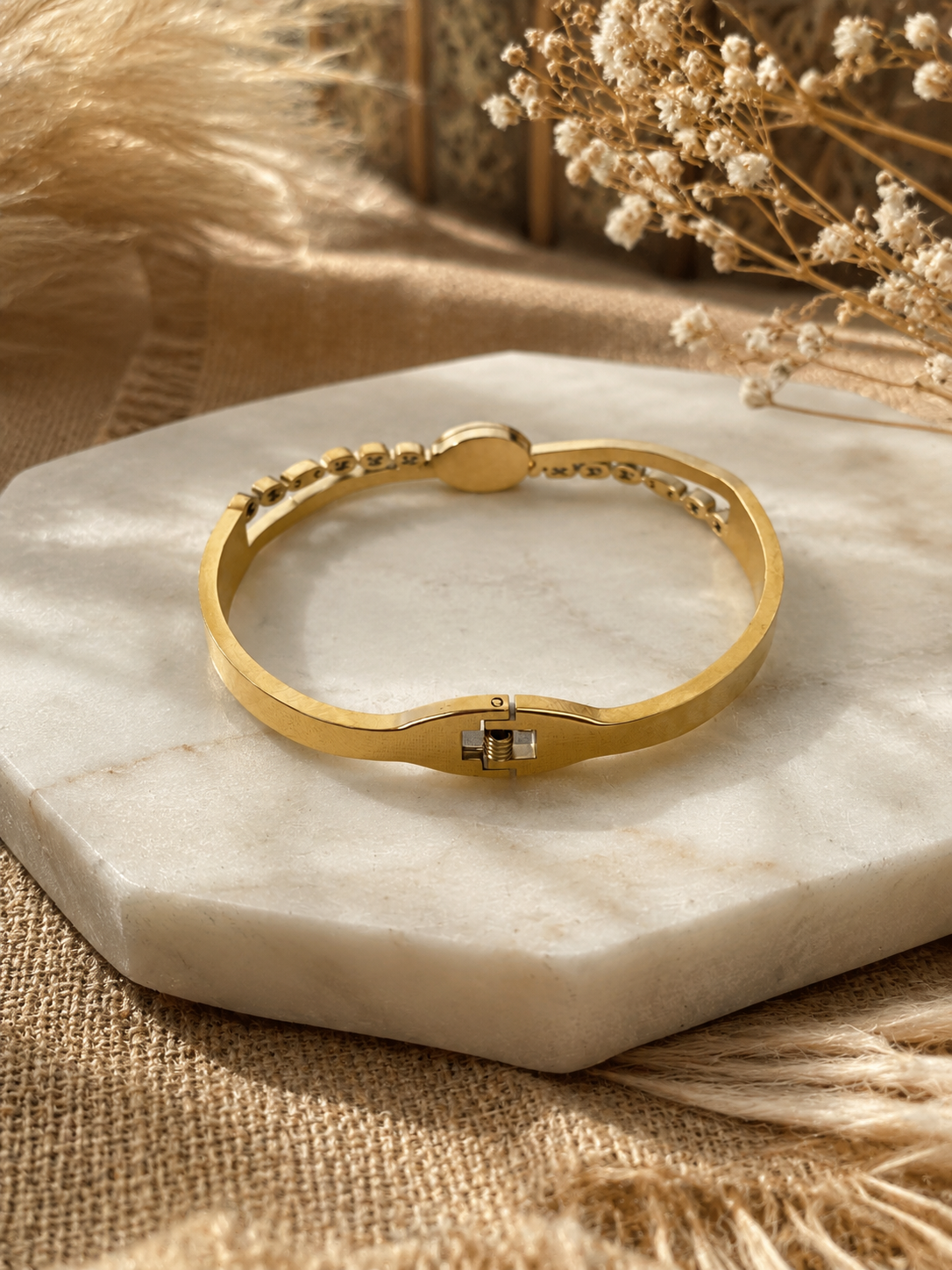 Gold bracelet on a marble surface with dried flowers in the background