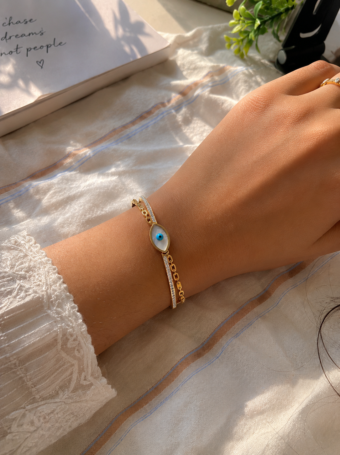 Hand wearing a gold bracelet with a blue stone on a textured surface.