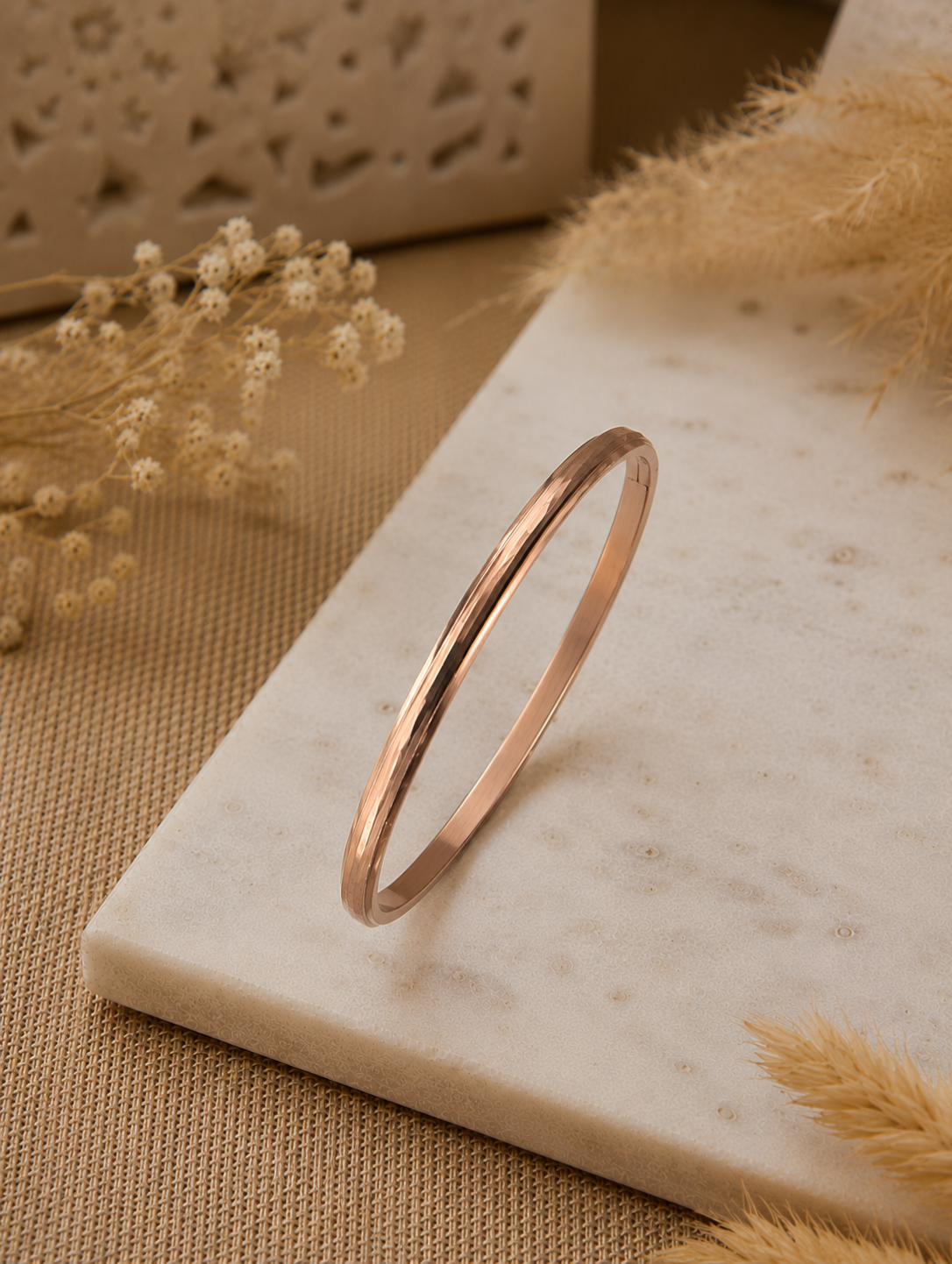 Antica Designs premium rose gold-toned hinged bangle featuring a multi-faceted geometric surface, showcased at an angle on a white marble slab.
