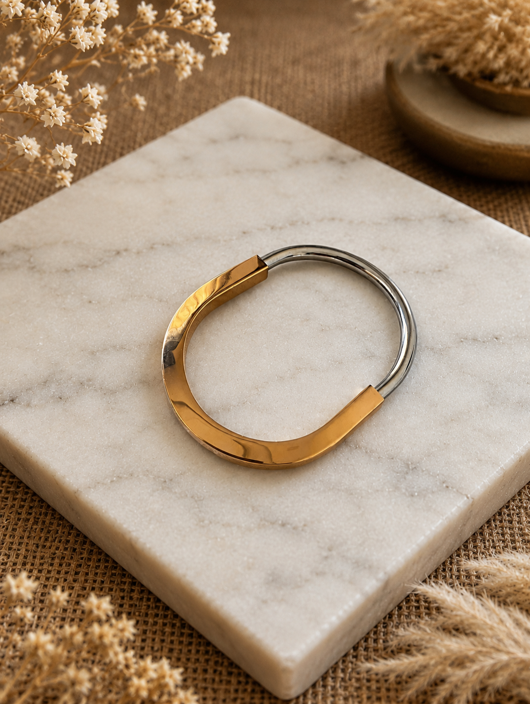 Antica Designs premium two-tone Bivara bangle showcasing a thick, high-polish gold crescent joined with a polished silver arch, displayed on a square white marble block