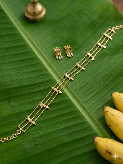 A traditional gold jewellery set featuring a three-layered delicate choker necklace and matching stud earrings with small dangling accents, elegantly displayed on a fresh green banana leaf.