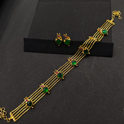 Gold bracelet with green gemstones and matching earrings on a black background