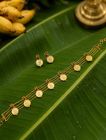 A traditional South Indian gold jewelry set, featuring a three-layered Kasu Mala choker necklace and matching stud earrings adorned with Goddess Lakshmi coins and small red ruby gemstones, displayed on a fresh green banana leaf with water droplets.