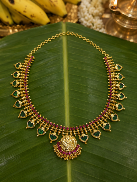 Kerala traditional Palakka jewelry piece displayed on a banana leaf, featuring a full-ruby variant with Green leaf-shaped stones and an intricate gold Lakshmi pendant.