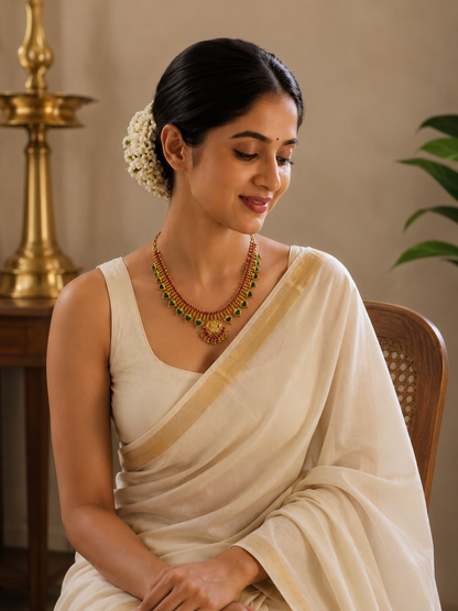 Portrait of a woman in elegant Kerala attire showcasing the traditional green stone Palakka necklace with pink ruby detailing and a round gold Lakshmi pendant.